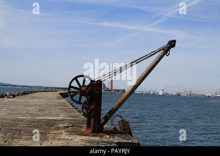 The rusty winch originally used to haul up food for for the Poolbeg lighthouse keepers with the chimneys of the old power station and Dublin Port Stock Photo