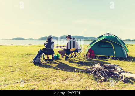 Group of travelers camping and doing picnic and playing music together. Mountain and lake background. People and lifestyle. Outdoors activity and leis Stock Photo
