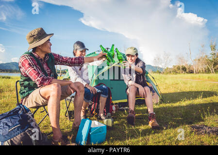Group of travelers camping and doing picnic in meadow with tent foreground. Mountain and lake background. People and lifestyles concept. Outdoors acti Stock Photo