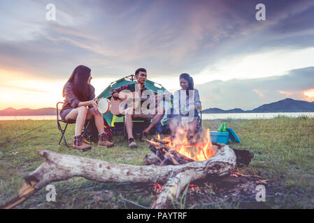 Group of travelers camping and doing picnic and playing music together. Mountain and lake background. People and lifestyle. Outdoors activity and leis Stock Photo