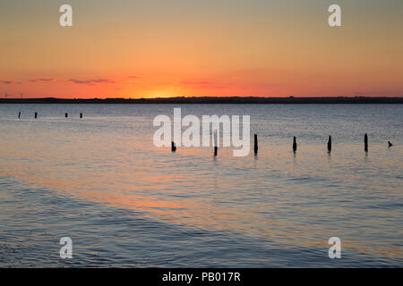 Vibrant orange sunset during the Solstice taken from Seasalter beach, Whitstable looking across the Swale Estuary on the North Kent coast, UK. Stock Photo