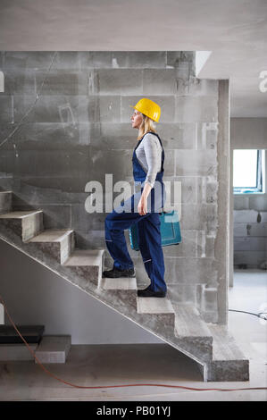 Woman worker with a tool box walking up the stairs on the construction site. Stock Photo