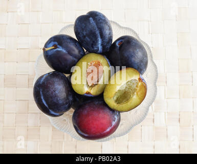 Few whole ripe and fresh violet plums in the bowl with one halved plum on the top Stock Photo