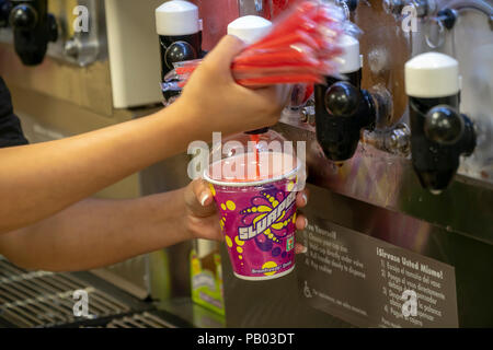 A worker fills a Slurpee in a 7-Eleven store in New York on Wednesday, July 11, 2018 (7-11, get it?), Free Slurpee Day! The popular icy, slushy, syrupy drinks are available in regular and diet flavors, in combinations, and the stores have stocked up with extra barrels of syrup to meet the expected demand. According to the meticulous figures kept by 7-Eleven they sell an average of 14 million Slurpees a month and over 150 million Slurpees a year.  (© Richard B. Levine) Stock Photo