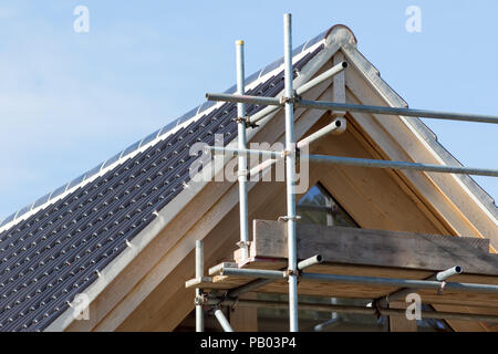 Modern house roof construction. Black curved ceramic tiles with scaffolding on the front of an expensive new build home. Stock Photo