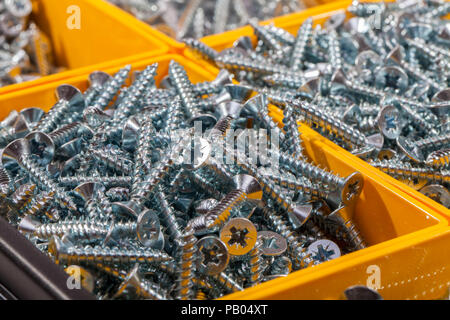 Woodscrews. Pile of cross head wood screws sorted in yellow box storage container. Assortment of silver DIY woodscrews in close up. Stock Photo