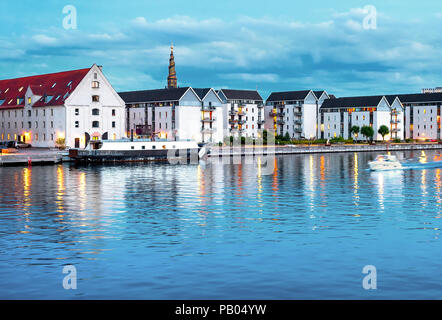 Residential houses buildings by embankment of Copenhagen illuminated in the evening,  Christianshavn Church of Our Saviour on background, Denmark Stock Photo