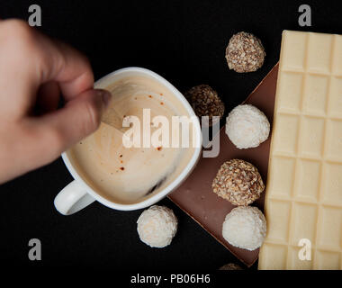 Woman adding sugar in coffee in cafe. Cofe, Stack of Black and White Chocolate isolated on black background, place for text. Stock Photo