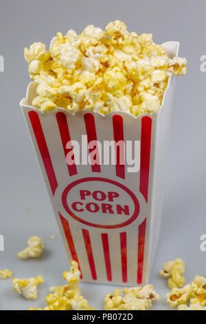 A red stripped popcorn small bucket overflowing with popcorn on a white counter Stock Photo