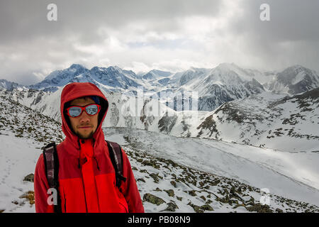 Selfi male mountaineer in snowy mountains, wearing a helmet with a backpack. Stock Photo