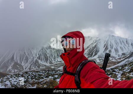 Selfi male mountaineer in snowy mountains, wearing a helmet with a backpack. Stock Photo