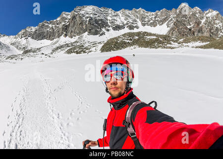 Selfi male mountaineer in snowy mountains, wearing a helmet with a backpack. Stock Photo