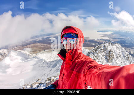 Selfi male mountaineer in snowy mountains, wearing a helmet with a backpack. Stock Photo