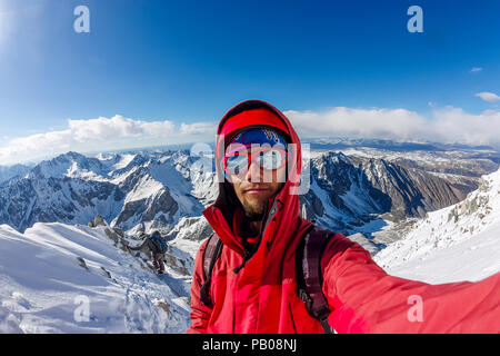 Selfi male mountaineer in snowy mountains, wearing a helmet with a backpack. Stock Photo