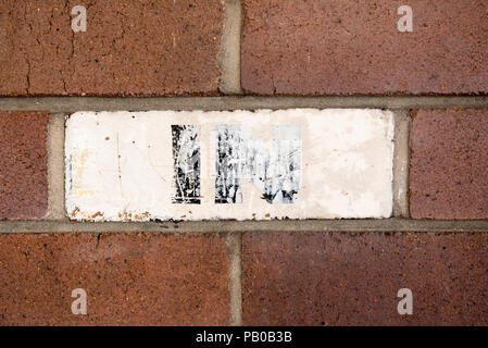 A faded hand painted IN sign with black letters on a white background painted over a face brick on a wall Stock Photo