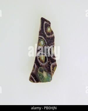 Glass mosaic bowl fragment. Culture: Roman. Dimensions: 1 9/16 × 9/16 × 1/16 in. (4 × 1.5 × 0.2 cm). Date: late 1st century B.C.-early 1st century A.D..  Translucent purple, light blue green appearing green, opaque white and yellow.  Concave curving side, thin-walled.  Mosaic pattern formed from polygonal sections of two canes: one in a purple ground with a white circle surrounding a central white outlined in green and yellow rings, and the other in a purple ground around a circular cluster of blue wedge-shaped rods outlined in yellow with a central white rod.  Polished interior; slight pittin Stock Photo