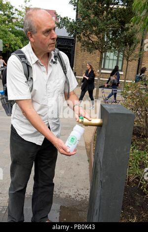 Man filling reusable water bottle from modern water fountain, Kings Cross, London Borough of Camden, England Britain UK Stock Photo