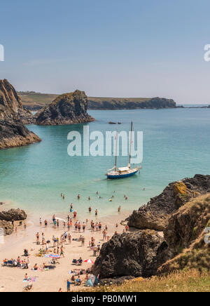 Summer in Cornwall- holiday makers at Kynance Cove on the Lizard Peninsular paddling around a yacht beached at low tide, UK Stock Photo