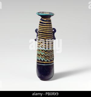 Glass alabastron (perfume bottle). Culture: Greek, Eastern Mediterranean. Dimensions: H.: 4 5/16 in. (11 cm). Date: late 6th-5th century B.C..  Translucent cobalt blue, with handles in same color; trails in opaque yellow and opaque turquoise blue.  Broad, uneven horizontal rim-disk, with slightly raised edge around mouth; short cylindrical neck; narrow rounded shoulder; straight-sided cylindrical body, tapering upwards; convex bottom; two vertical ring handles with knobbed tails, applied over trail decoration.  Turquoise blue trail attached at edge of rim-disk; a yellow trail applied on unders Stock Photo