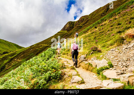 Hikers in summer clothes walking up the steep track to Loch Skeen from Grey Mare's Tail Nature Reserve in the Moffat Hills. Scotland, UK. Stock Photo