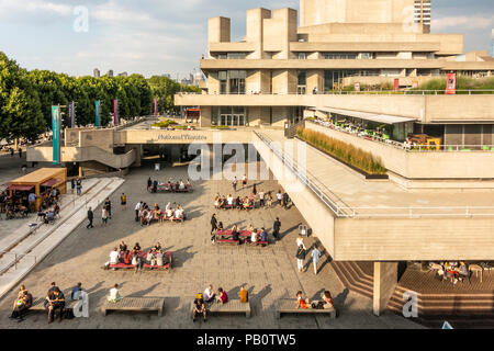 Tourists and locals enjoying a hot July evening outside the concrete Brutalist architecture of the National Theatre in London, UK