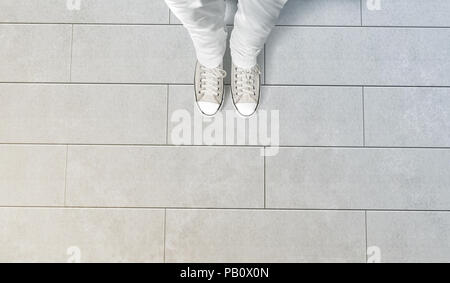 Person taking photo of his feet stand on concrete floor, isolated, top view, clipping path. Ground design mock up. Man wear gumshoes and watching down Stock Photo