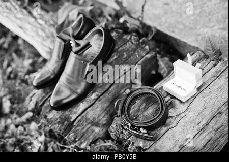 Close-up photo of groom's shoes, cufflinks, belt and bow tie on wooden surface. Black and white photo. Stock Photo
