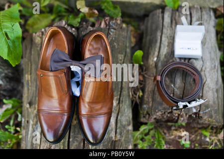 Close-up photo of groom's shoes, cufflinks, belt and bow tie on wooden surface. Stock Photo