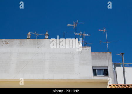 White side wall of a house with two traditional chimneys on the roof and several antennas. Bright blue sky. Vila Real de Santo Antonio, Algarve, Portu Stock Photo
