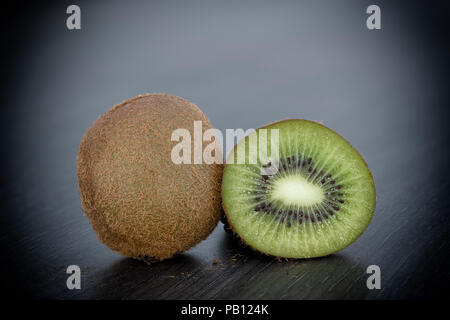 Close up of one whole and one sliced Kiwi fruit on a plain grey kitchen worktop with vignetting Stock Photo