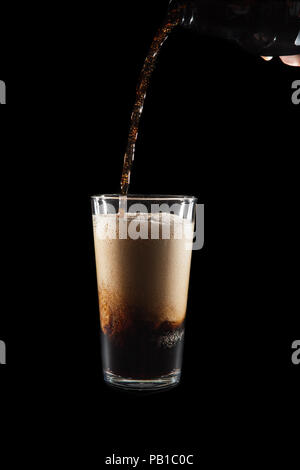 International Beer Day. Stout ale being poured in to a pint glass. Against black background with copy space. Stream of dark frothy stout beer flowing  Stock Photo