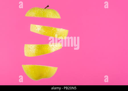 Pieces of an green apple flying in the air and space for sample text or design on pink background. Cut and levity fruit floating in the air concept Stock Photo