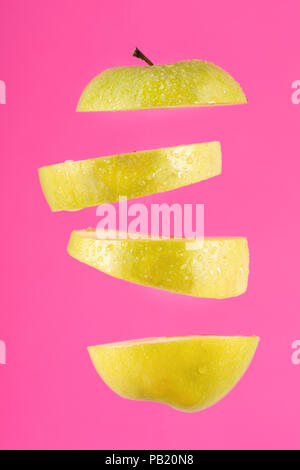 Fresh flying green apple cut with drop of water isolated on pink background. Levity fruit floating in the air concept Stock Photo
