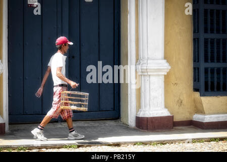 Man walking along street carrying a birdcage in Trinidad, Cuba Stock Photo