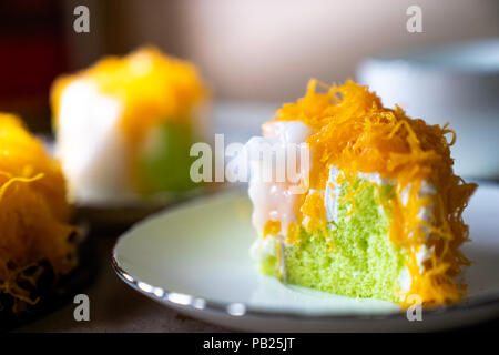 selective focus piece of  Gold Egg Yolk Thread Cake , or  'Cake Foi Tong' Thai pandan cake  with delicious young coconut cream on white plate Stock Photo