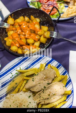 Lemon chicken with homemade fries, patatas bravas (Spanish fried potatoes) and chicken gyros with homemade chips and vegetable salad. Stock Photo