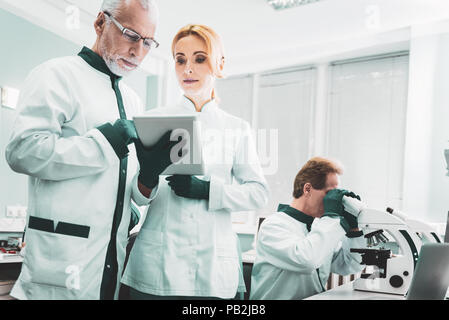 Two chemists standing near researcher using microscope Stock Photo