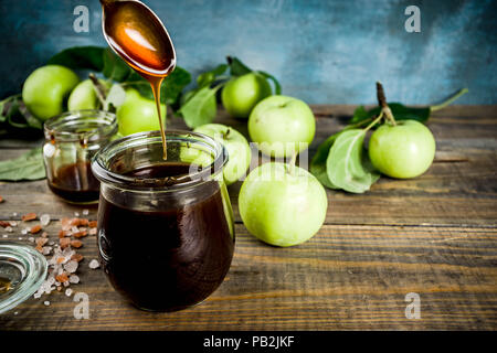 Home cooked dark salted classic caramel sauce, with green apples, wooden and dark blue background, Stock Photo
