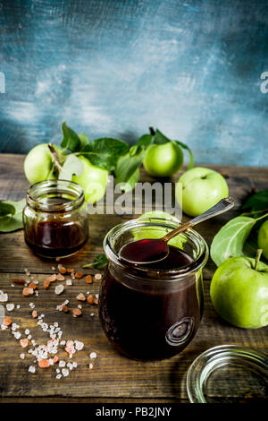 Home cooked dark salted classic caramel sauce, with green apples, wooden and dark blue background, Stock Photo