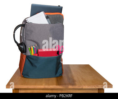 Heavily loaded backpack with school supplies on wooden table and isolated Stock Photo