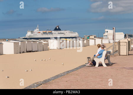 Calais, France - 19 June 2018: People sitting on a bench and looking at a DFDS cross Channel ferry leaving the port Stock Photo