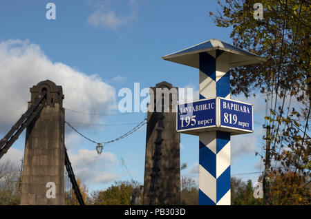 Milepost with names of the cities in Russian and distance in kilometers and with the suspension bridge on a background Stock Photo