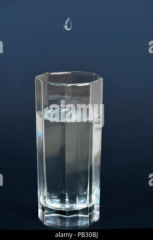 Drop of water or other liquid falling into a glass filled with a clear and cool refreshing drink Stock Photo
