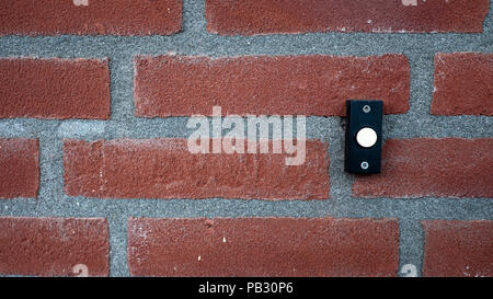 background of a red stone wall with a black with white doorbell button. Stock Photo