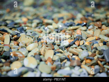 Waves of the sea washed pebbles. Smooth multi-colored stones sparkle in the sun. Stock Photo