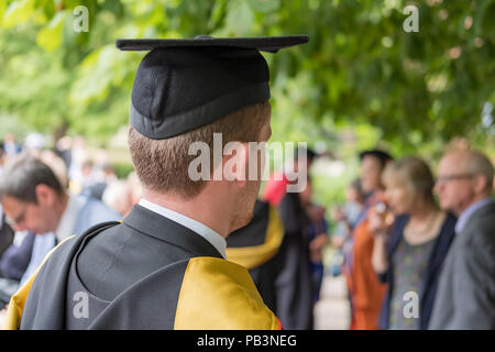 Young male graduated student seen his his graduation dress at a campus graduation  party shown various parents in the background Stock Photo - Alamy