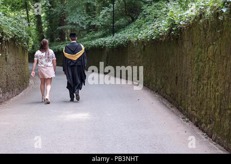 Young college couple seen walking down a campus path, following the young man's graduation ceremony. Stock Photo