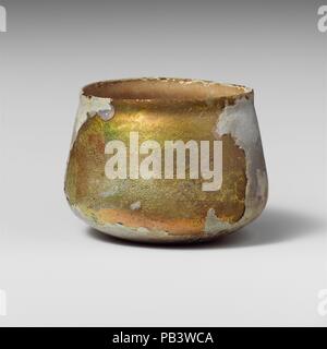 Glass cup. Culture: Roman. Dimensions: Overall: 2 5/8in. (6.6cm)  Diam.: 3 1/2 x 2 7/8 in. (8.9 x 7.3 cm). Date: 2nd-3rd century A.D..  Uncertain, probably colorless with greenish tinge.  Knocked-off, uneven rim; slightly bulging collar below rim; sides expanding downward, then angled in to join bottom with slightly concave center.  Band of faint wheel-abraded horizontal lines on body above angle.  Complete, but with large crack from rim down side to bottom; many pinprick bubbles; deep pitting and brilliant iridescent weathering on exterior; thick, creamy brown weathering on interior. Museum:  Stock Photo