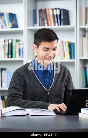 Happy student is learning in library. He is using laptop. Stock Photo