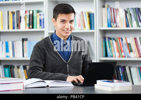 Happy student is learning in library. He is using laptop. Stock Photo